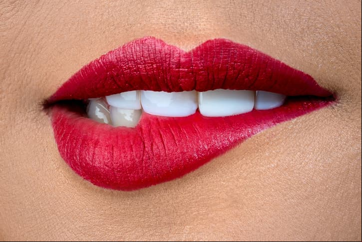 Close-up on a woman biting her red lips - makeup and beauty concepts