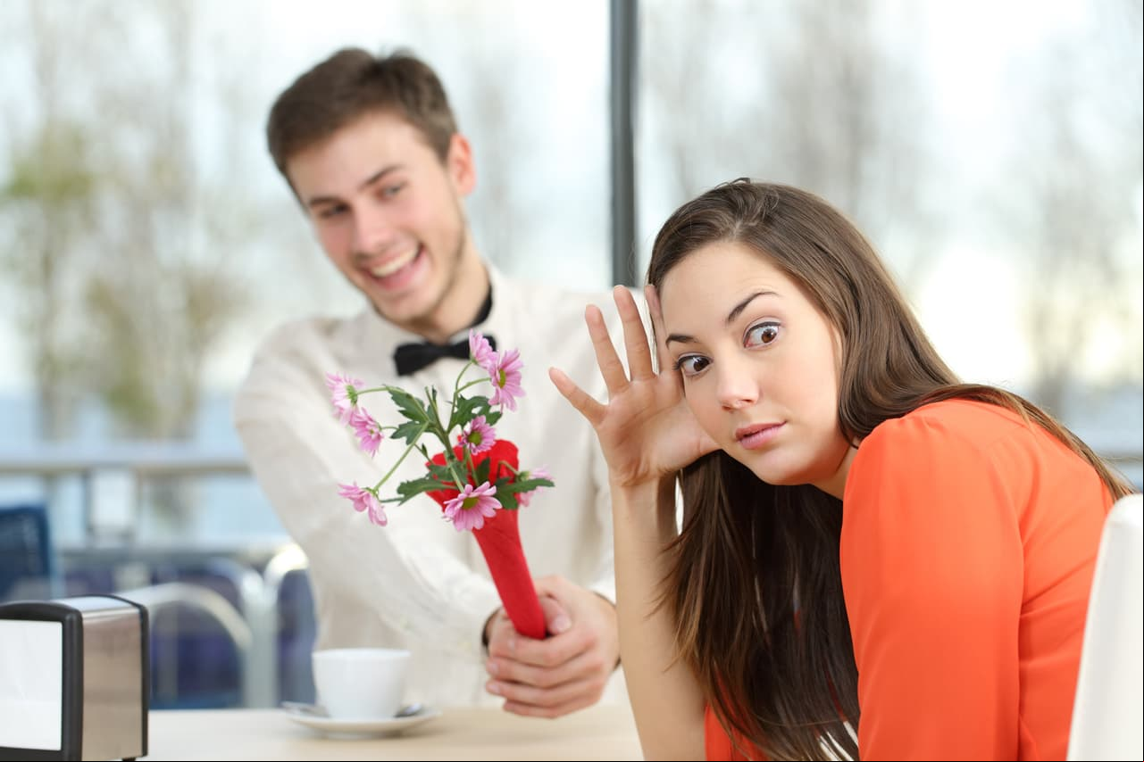 Disgusted woman rejecting a geek boy offering flowers in a blind date in a coffee shop interior