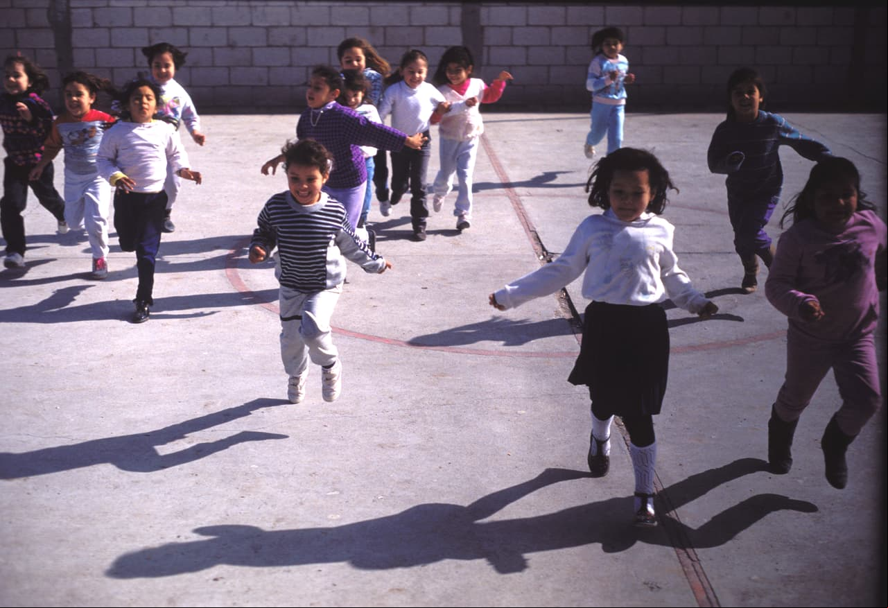 Boys and girls run in the schoolyard, Juarez, Mexico, late 1980s. (Photo by Mark Jay Goebel/Getty Images)