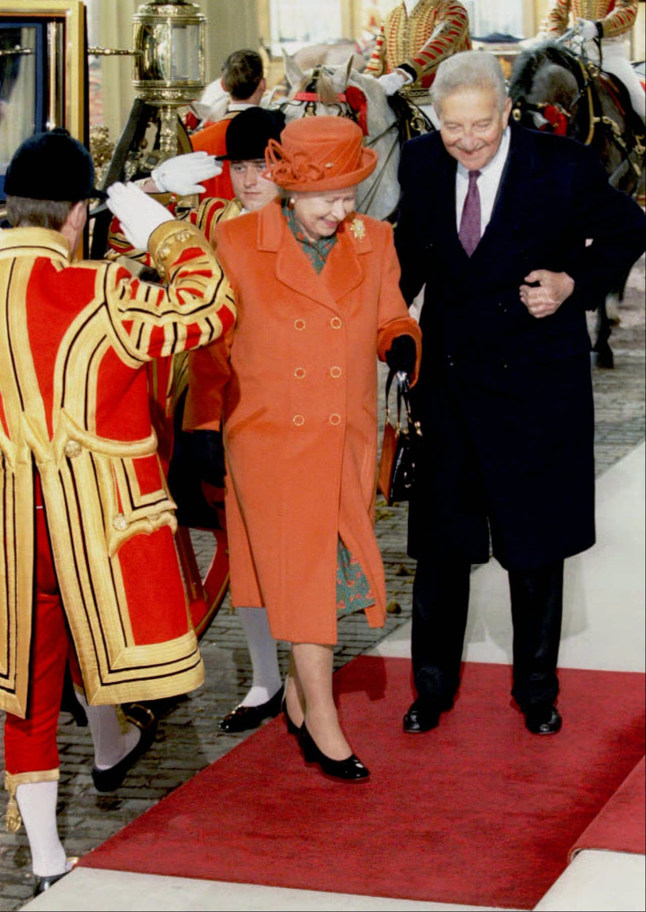 El color naranja no podía faltar en su armario, por ello la Reina Isabel II optó por un abrigo y sombrero de ese tono para su llegada al palacio de Buckingham en 1997.