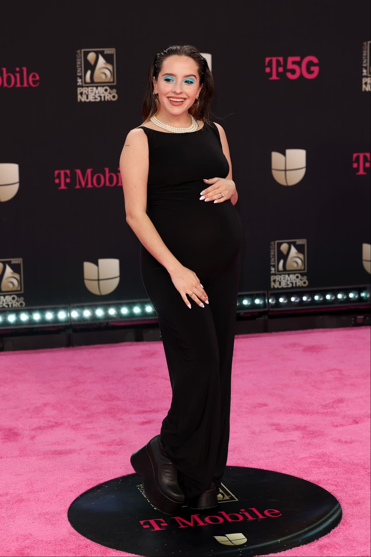 Evaluna Montaner: Con vientre abultado y acompañada de Camilo, la cantante desfiló en un vestido negro clásico, y unos cómodos zapatos de plataforma. Para añadir aún más elegancia al outfit, Evaluna añadió un collar en cascada de perlas y el toque estrella: sombras azul aqua.
